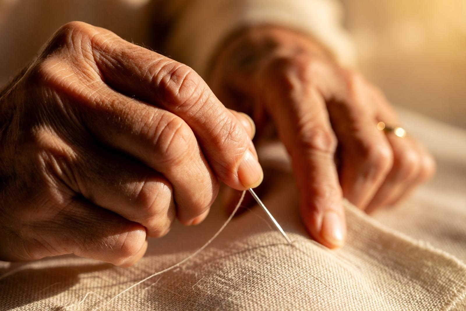 Welvin's hands pulling needle and thread through fabric in warm studio light