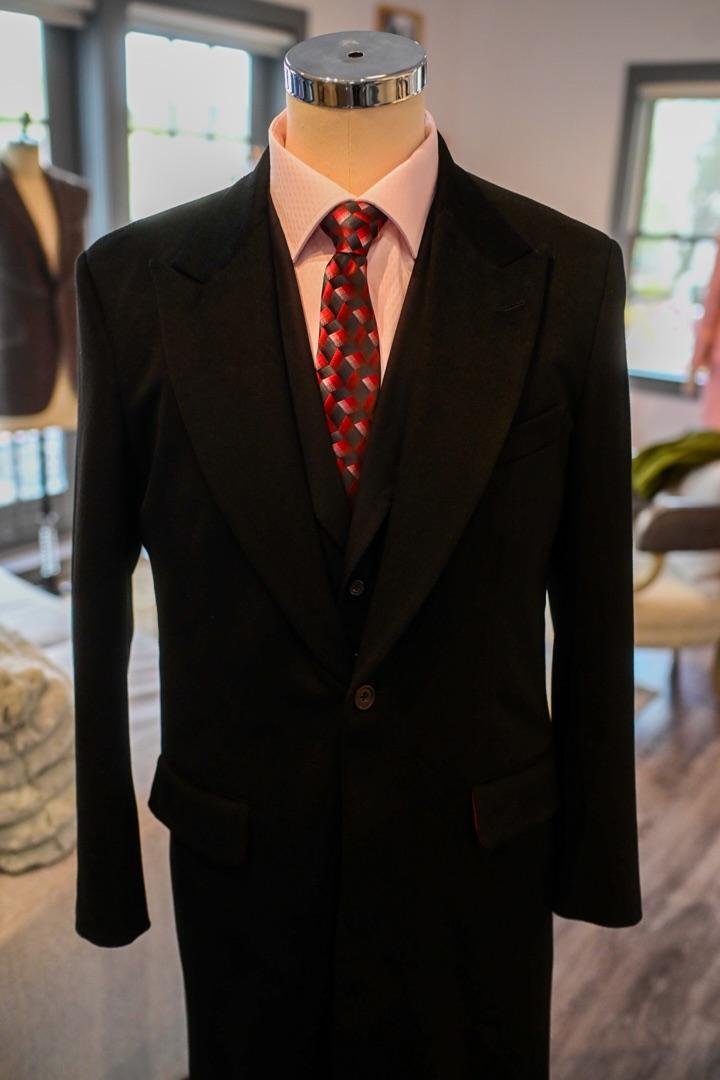 Full-length black bespoke overcoat on dress form with pale pink dress shirt and red geometric silk tie