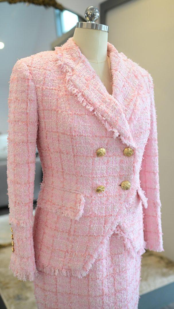 Pink bouclé tweed women's bespoke jacket with gold double-breasted buttons and fringed lapels hanging on a dress form
