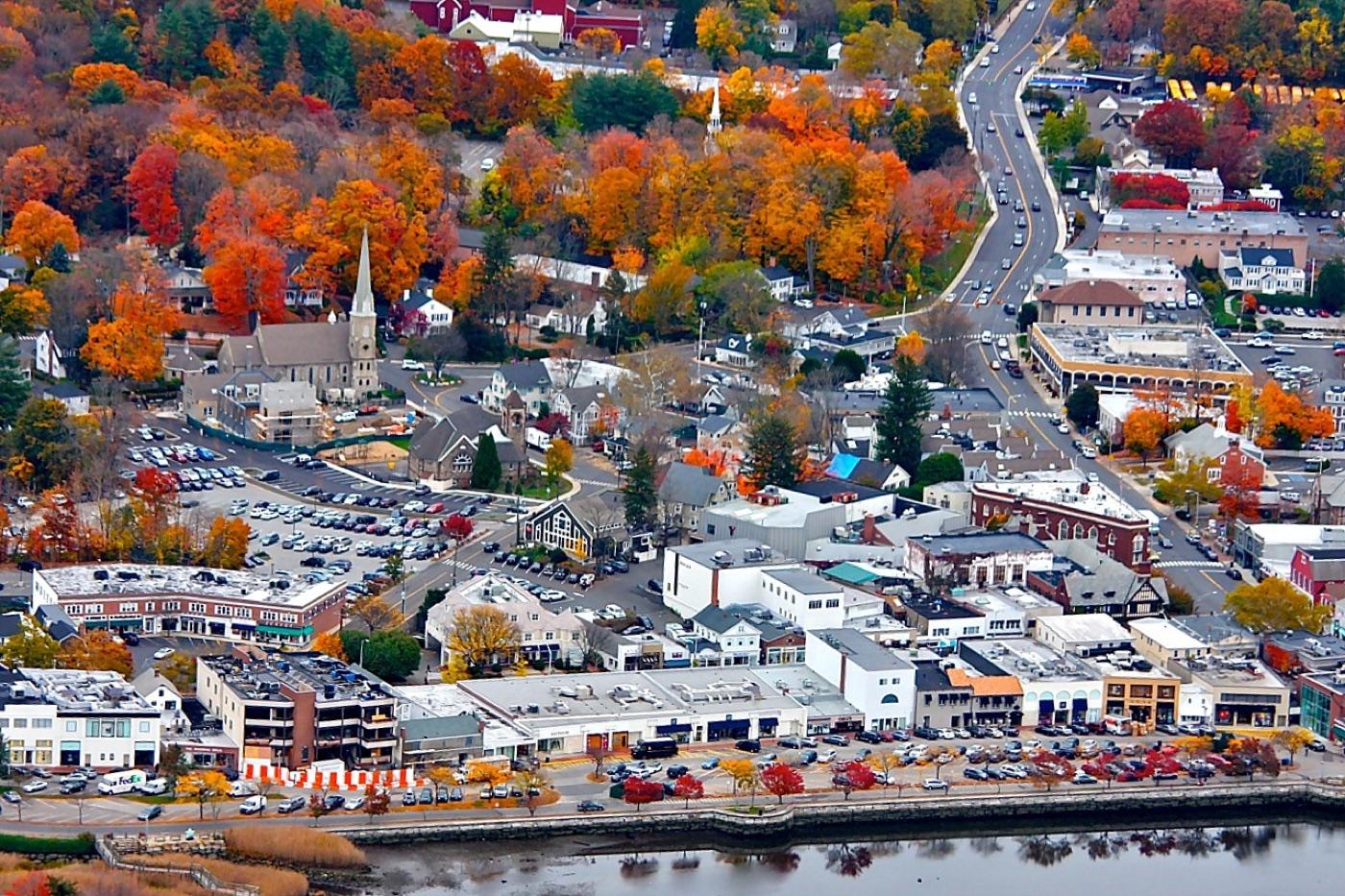 Aerial view of Westport, CT in autumn — Main Street shops, the white church steeple, and the Saugatuck River in the foreground